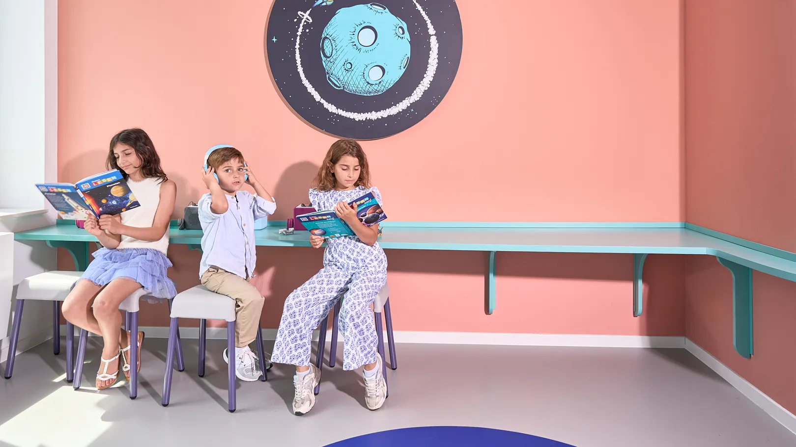 Wartebereich mit Leseecke – RKM 740 Kinderzahnheilkunde Düsseldorf Kinder lesen im Wartebereich der RKM 740 Kinderzahnheilkunde in Düsseldorf unter einem Wandmotiv mit Mond